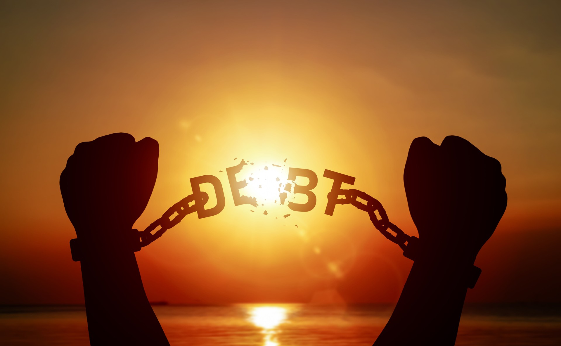 Silhouette of raised hand pulling a chain with word DEBT on until it breaks. Concept of debt relief, freedom from debt.